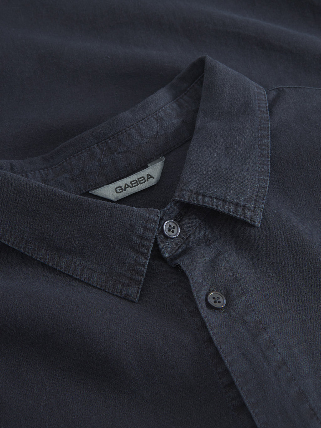 Close-up of the Sven Reg Lino LS - Night Sky from Gabba, featuring a dark blue button-up design with a collar. The soft, slightly textured fabric offers comfort, while two visible buttons on the front placket highlight the shirts premium detail.