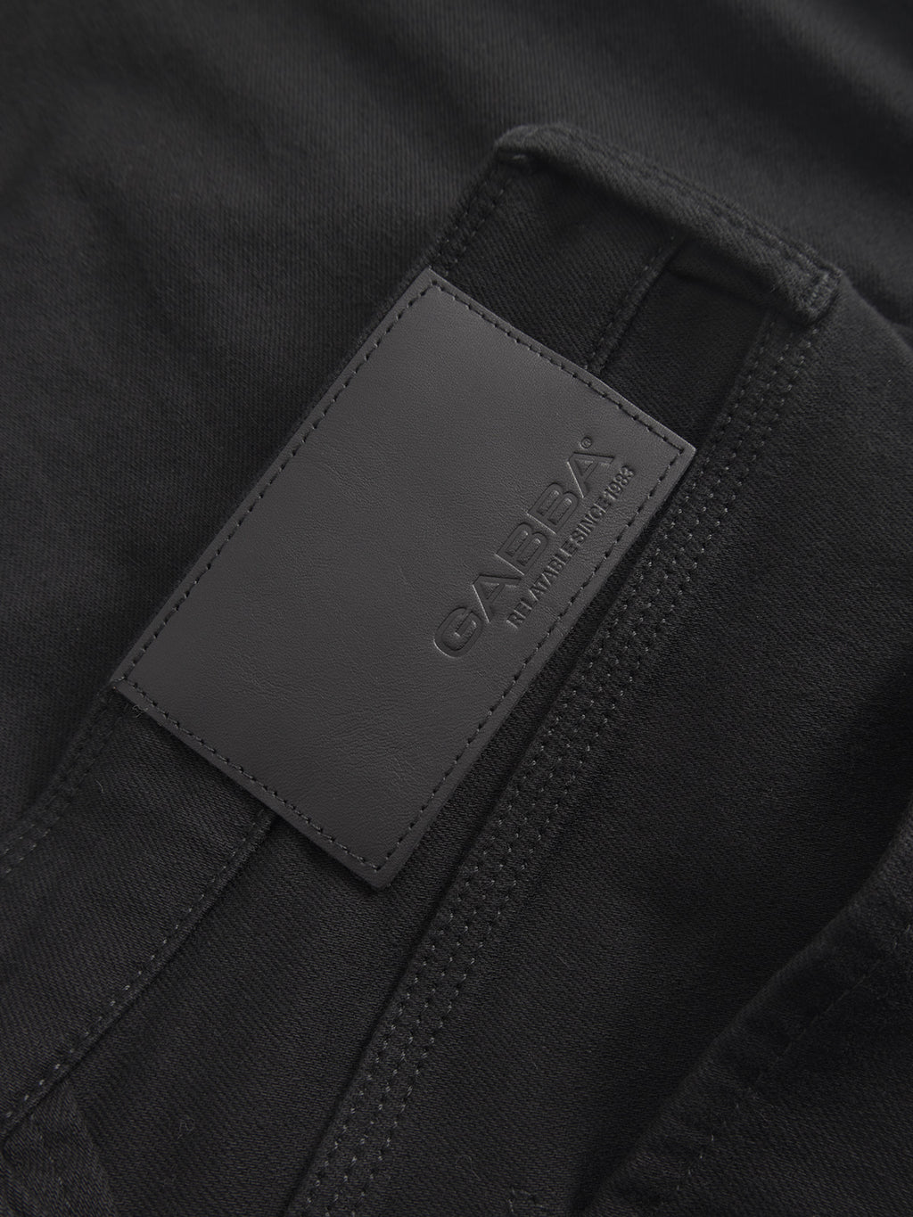 Close-up of a sleek black wash fabric featuring a rectangular label embossed with Gabba and smaller text. It hints at the modern slim fit and refined style of the Max Sword - Black Denim.
