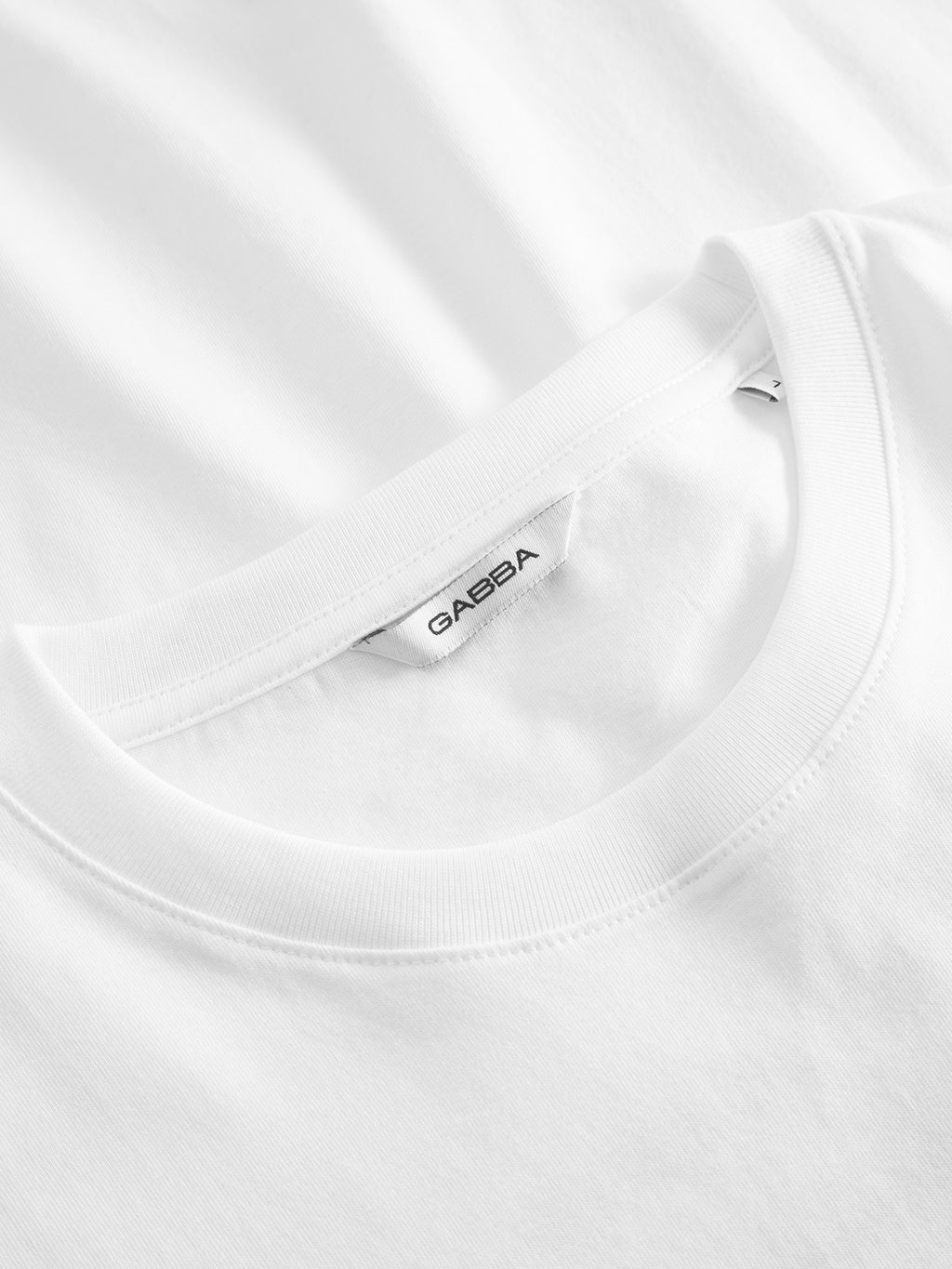 Close-up of GABBAs Dune Kiosk A SS GOTS - White T-shirt with a round neckline. The inner label, in black text on white, displays Gabba. Made from organic cotton, the soft fabric is well-stitched.