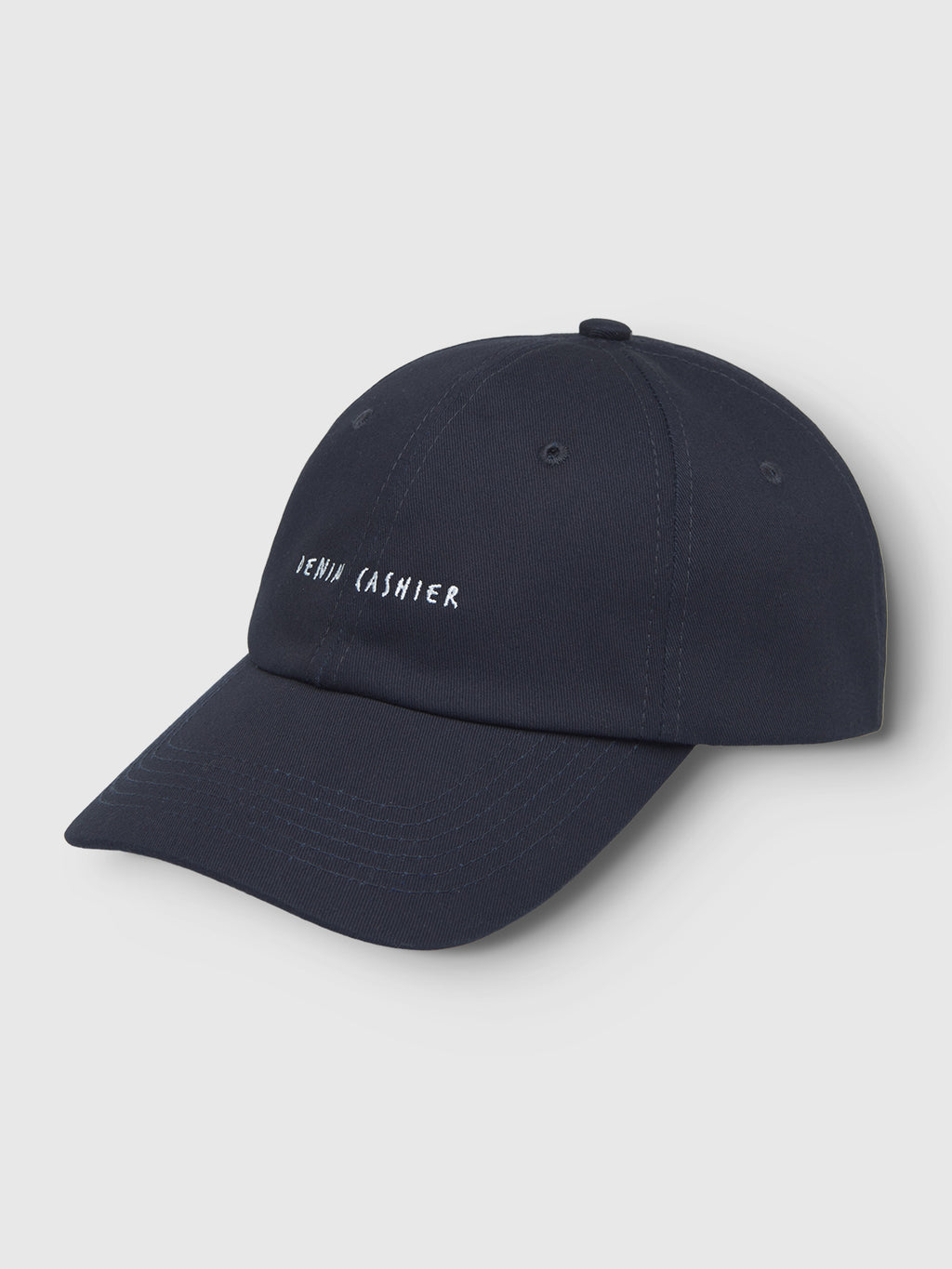The Gabba Cashier Cap - Night Sky is a dark blue cotton baseball cap featuring a white embroidered JENNA CASHIER logo. Made from durable twill, its sleek design stands out against a light gray background.
