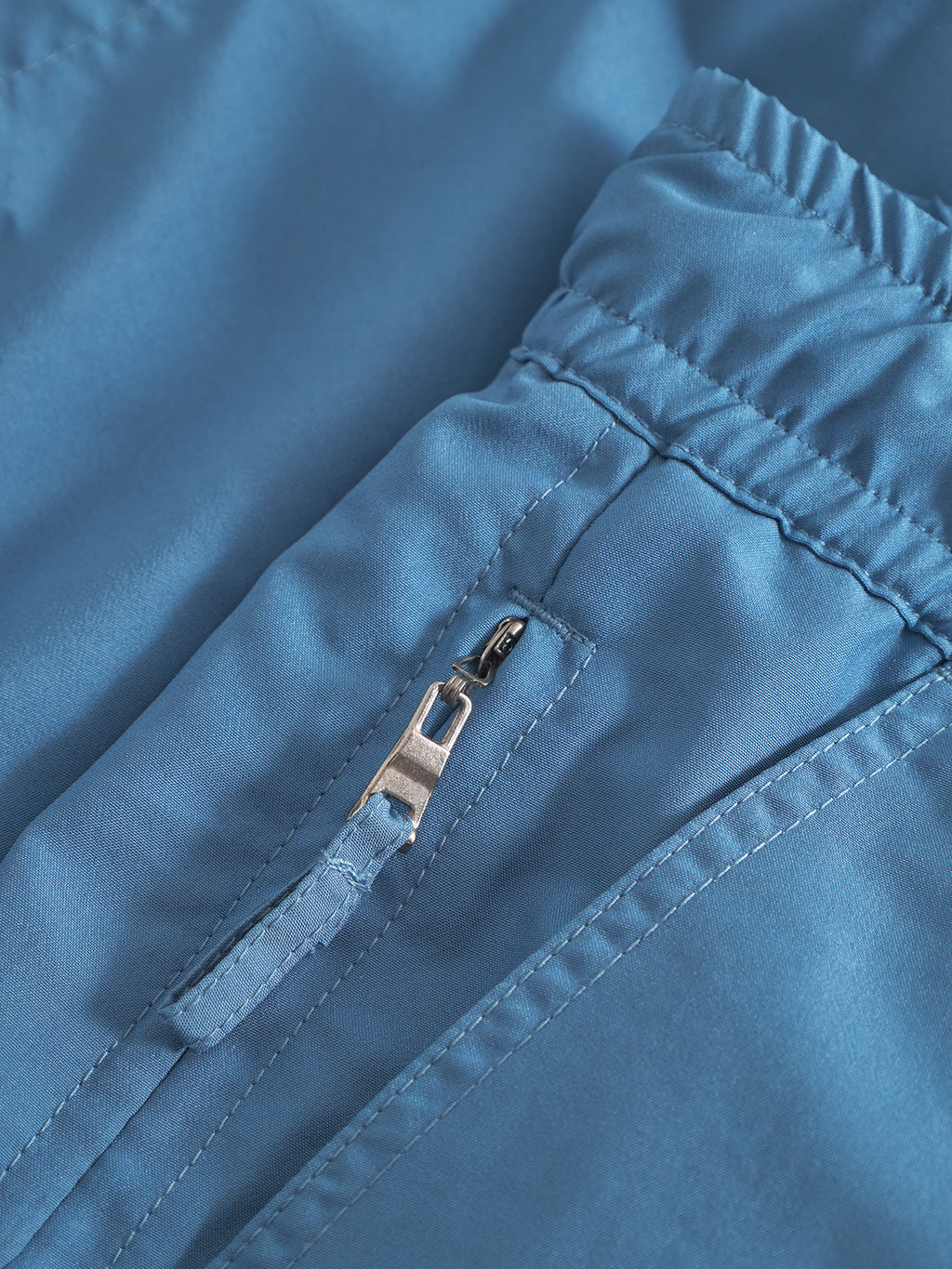 Close-up of Gabba Jackson Plain swim shorts in Blue Horizon, featuring an elastic waistband and a zippered side pocket with a silver zipper pull.