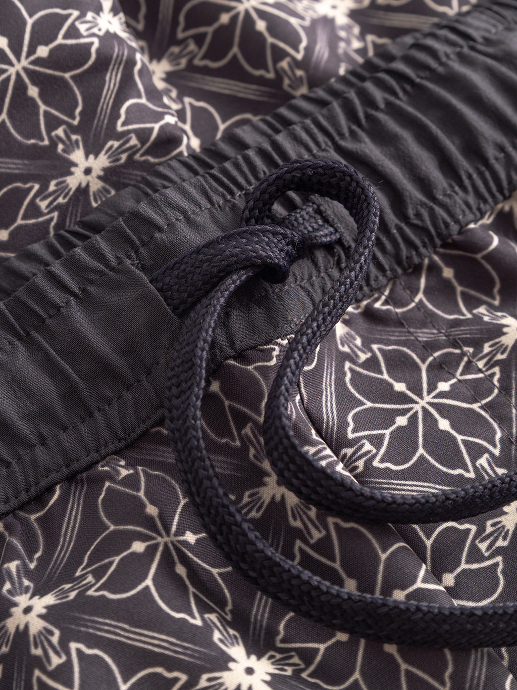 Close-up of Gabbas Jackson Print - Multi Pattern swim shorts, featuring a dark color with white floral print, elastic waistband, tied drawstring, and side pockets.