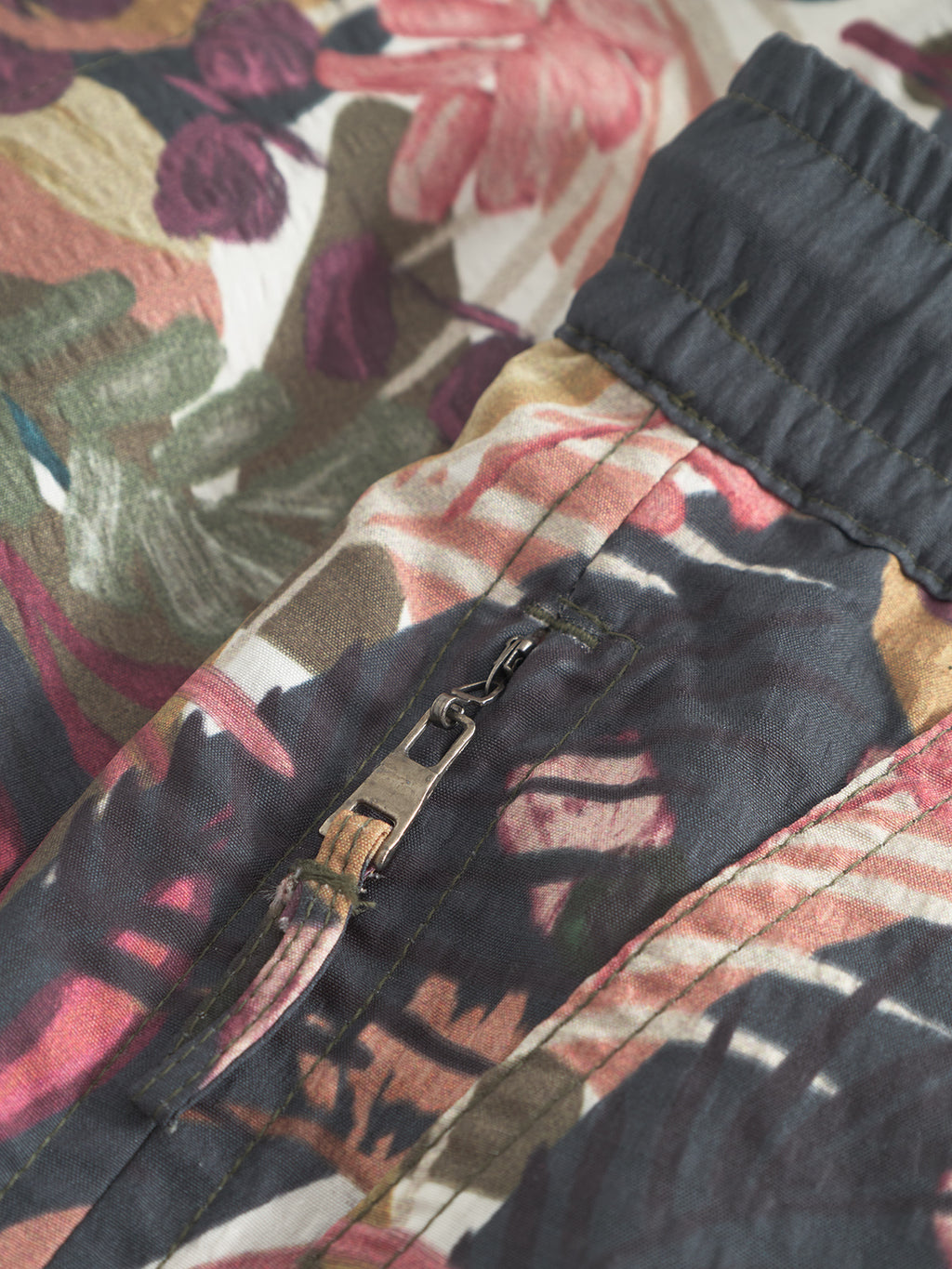 Close-up of Gabba’s Jackson Seer Print - Flower Mix swim shorts, showing their vibrant floral pattern, side pocket with a partially open metal zipper, and contrasting dark stitching along the edge.