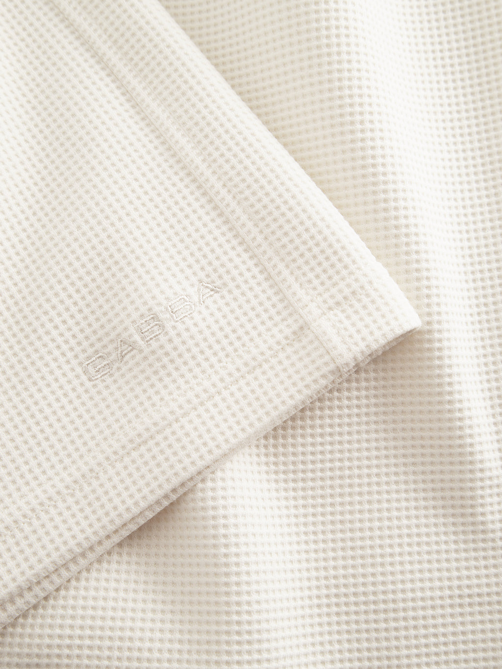 A detailed view of the Tim Waff - Bone White by Gabba reveals a textured waffle fabric with a white pattern, perfect for premium shorts. The corner displays an embossed CASA logo, highlighting comfort and durability.