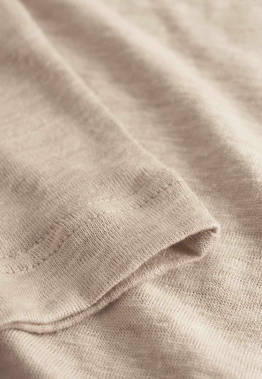 A close-up of the Trevor - Sand Plaza fabric by Gabba reveals a neatly stitched hem, showcasing its soft, slightly ribbed texture. The premium t-shirt material offers superior comfort with subtle shading variations, highlighting its fine detailing and craftsmanship.