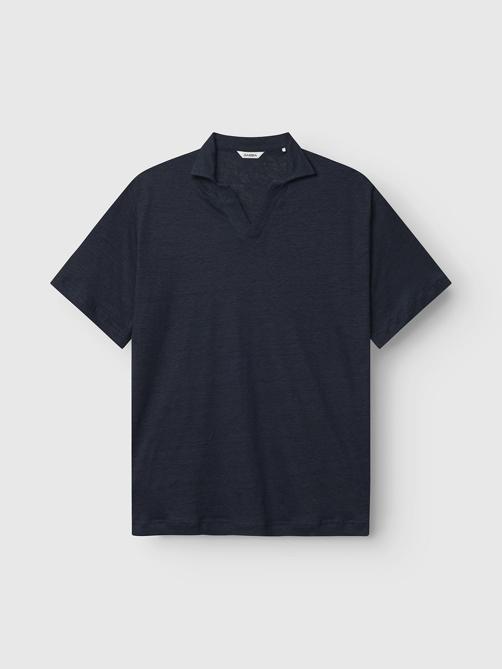 The Trevor - Navy by Gabba is a dark navy short-sleeve polo with a minimalist design, featuring a subtle V-neck collar. Made from linen, it offers exceptional comfort and a textured, premium feel, displayed against a plain light gray background.