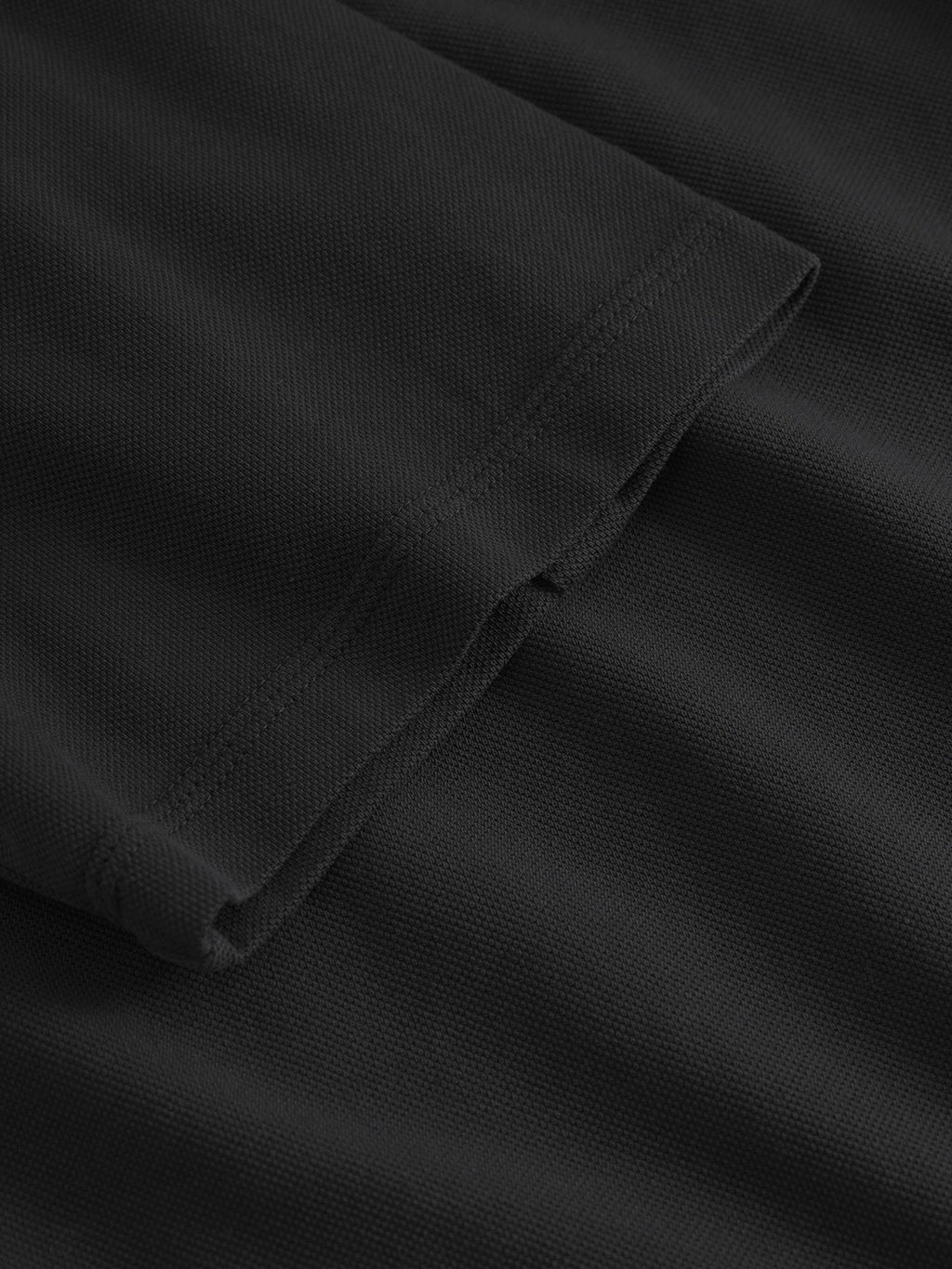 The Neo Pique Resort SS - Meteorite by Gabba showcases a folded black fabric with a textured woven pattern for ultimate comfort. The smooth hemline with even stitching highlights precision, capturing Gabbas dedication to personal style.
