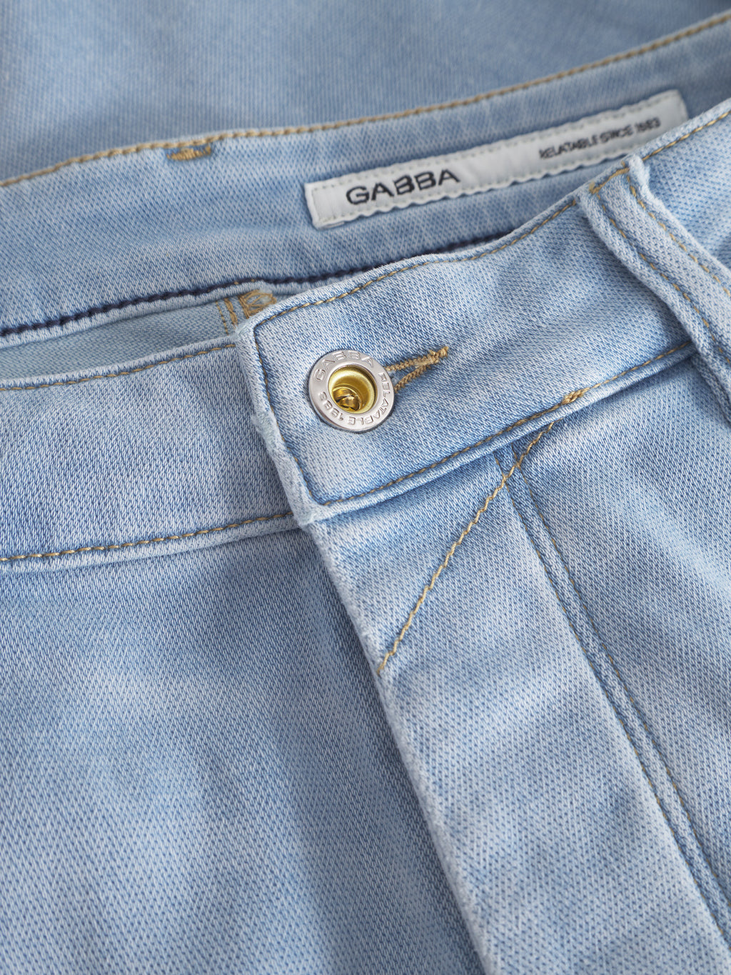 Close-up of Jason K3787 SANZA Shorts in light blue denim, highlighting the button and waistband. The Gabba label tag is visible, and the knee-length design is made from super-stretch fabric with a classic textured denim weave.