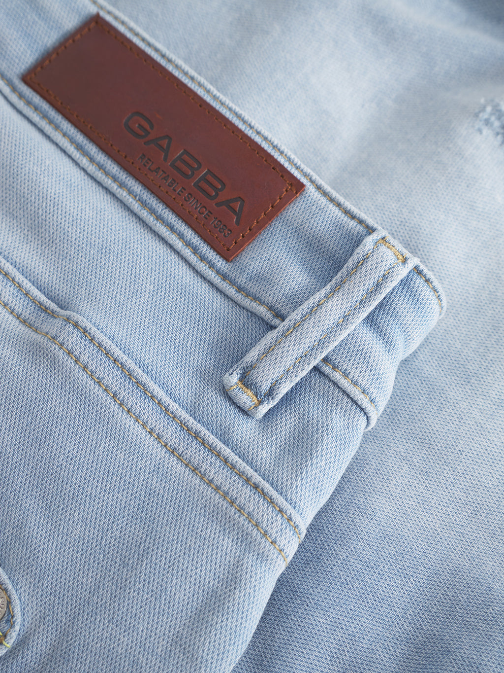 A close-up of the Jason K3787 SANZA Shorts in light blue denim shows a brown leather patch labeled Gabba, with visible stitching and belt loops that accentuate the super-stretch fabrics texture and design on these knee-length shorts.