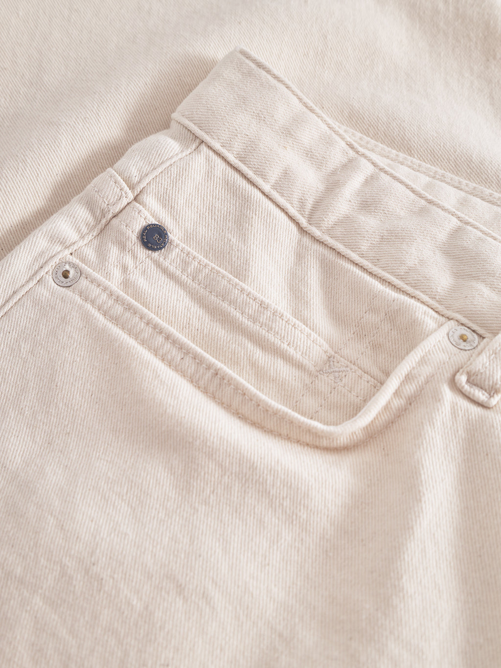 A close-up of the back pocket on Gabbas Maxwell Luis Cargo Shorts in ecru reveals a button detail on the small pocket. The textured, ribbed non-stretch fabric is perfect for workwear, with classic stitching and metal rivets bolstering corner durability.