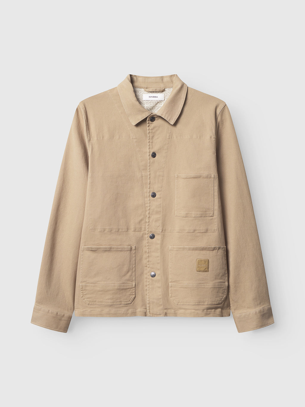 The Gabba Beta Twill - Sand is a beige cotton chore jacket in garment dyed twill, featuring a collar, button-down front, long sleeves, and three large front pockets, shown against a plain white background.