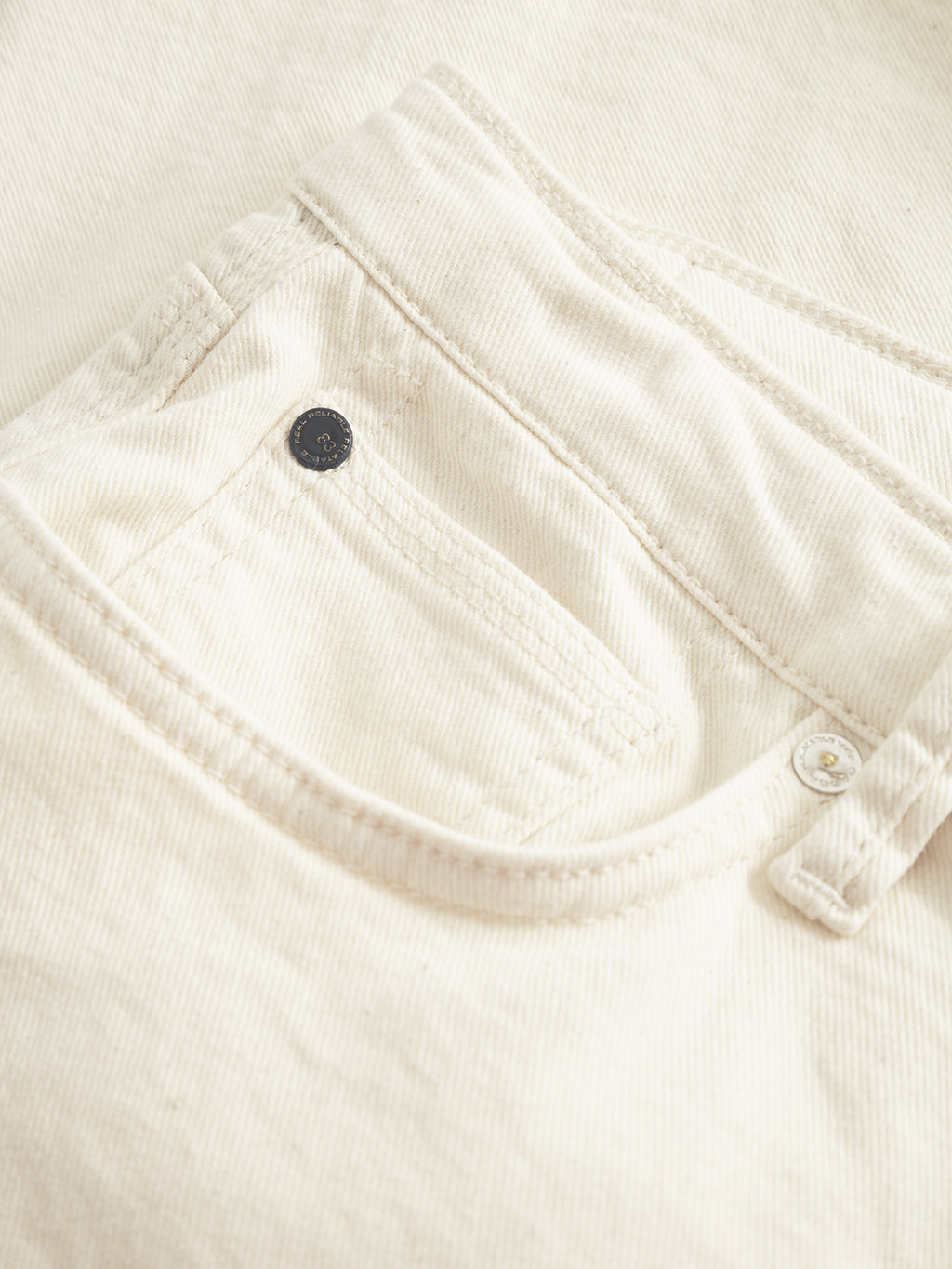 A close-up reveals the front pocket and button detail of the Maxor Luis Shorts in ecru by Gabba, capturing the vivid texture. The comfort stretch fabric ensures ease of movement, making these shorts both stylish and flexible.
