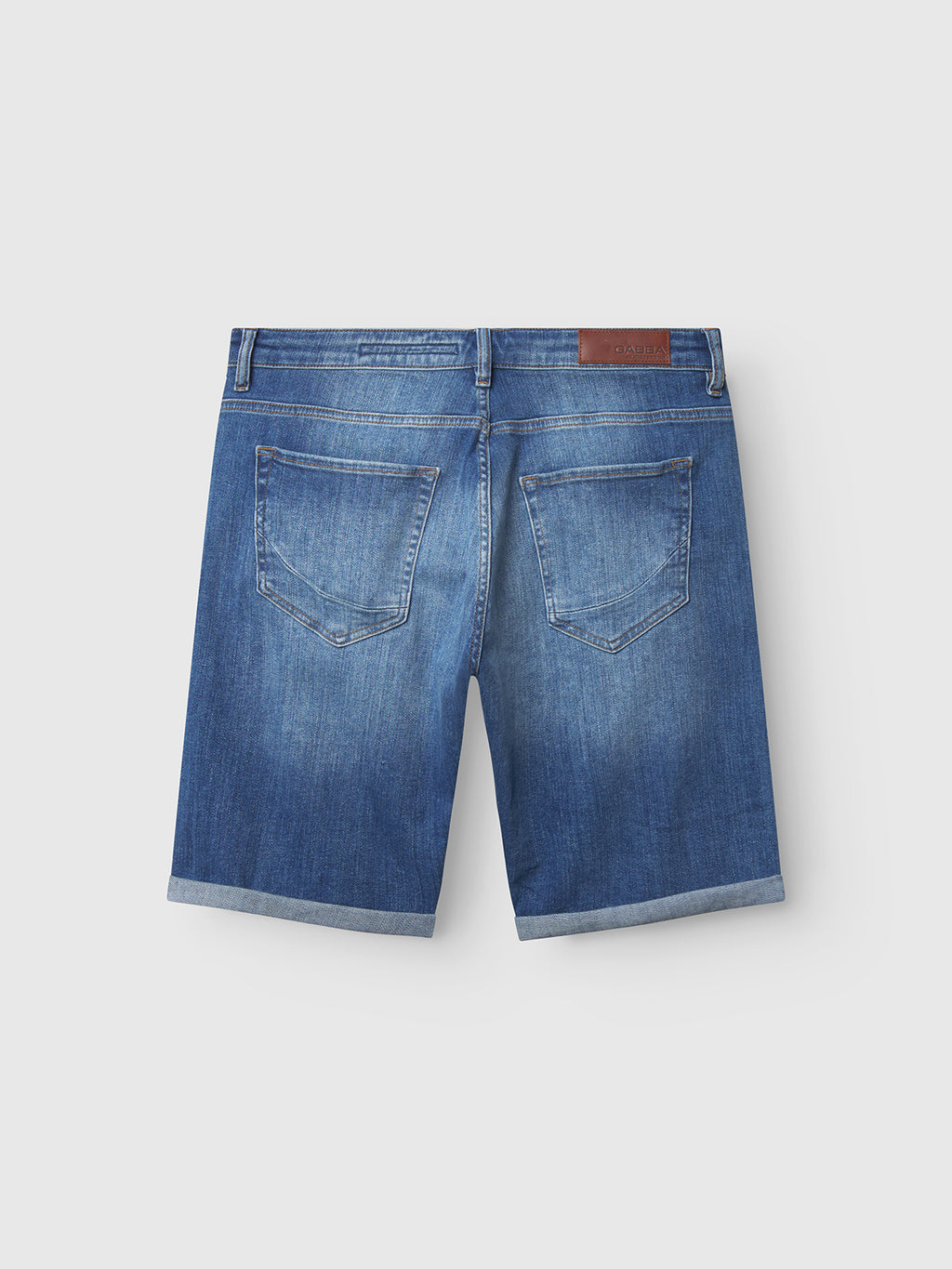 The Markus Selvedge Shorts Limited in Mid Blue Denim by Gabba feature a comfortable back view with two back pockets, a rolled hem, and a brown leather patch on the waistband. Crafted from recycled viscose, they are shown against a plain light background.