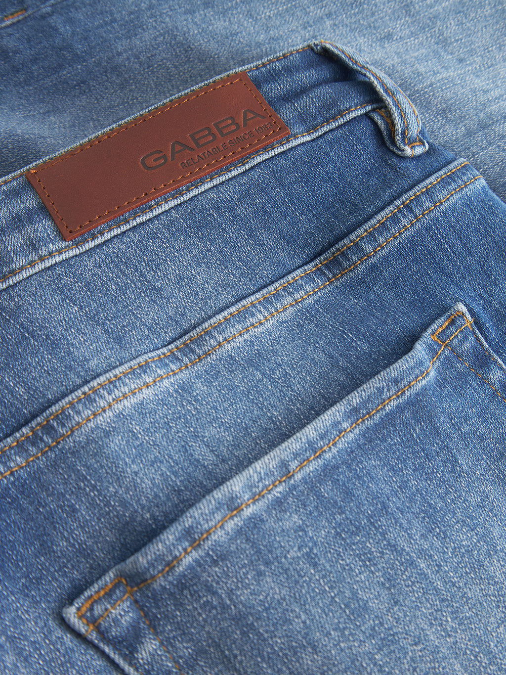 Close-up of Gabba Markus Selvedge Shorts Limited in mid blue denim, showcasing a leather patch with the brands embossing above the back pocket. Visible stitching highlights the texture and details, promising comfort and style.
