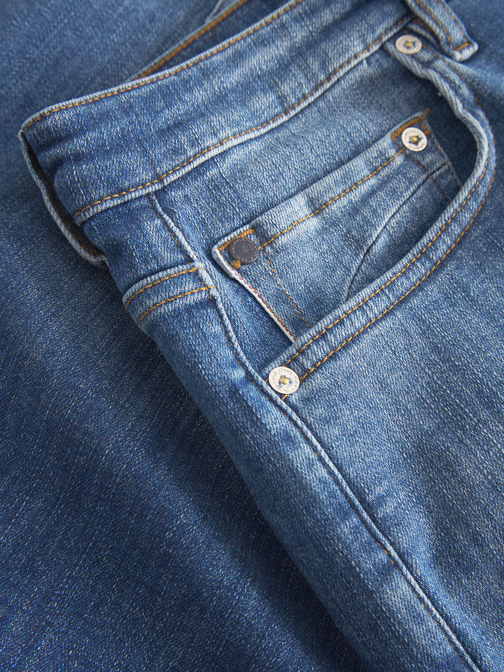 Close-up of Gabbas Markus Selvedge Shorts Limited in mid blue denim, highlighting the front pocket, button, and stitching. The recycled viscose fabric shows a slightly worn look typical of blue jeans, for that comfortable fit we all adore.