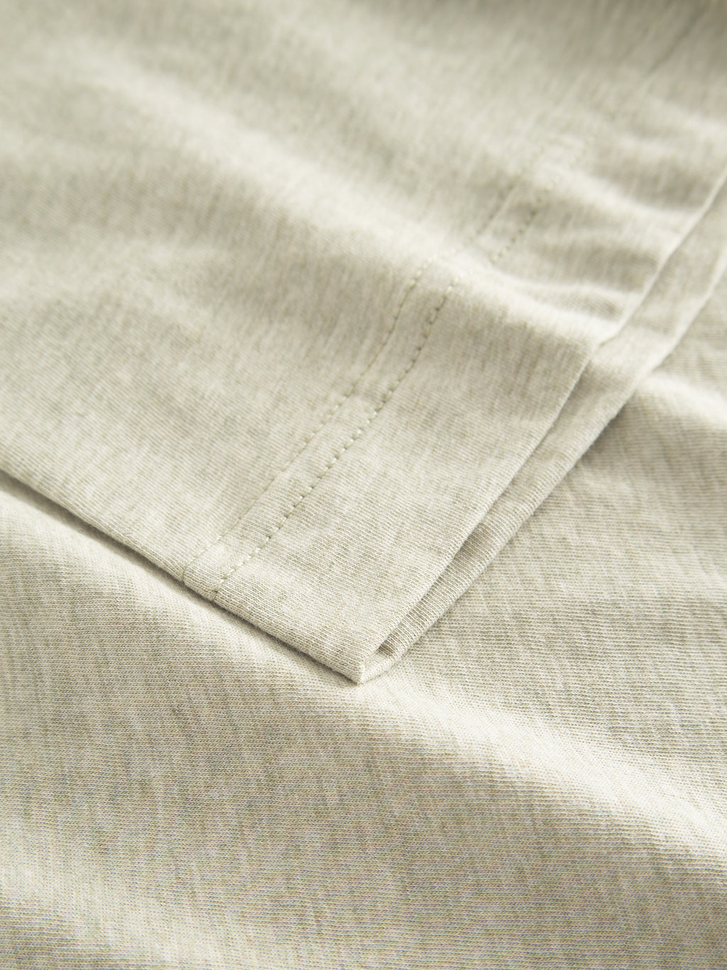 Close-up of neatly folded green melange jersey fabric, showcasing its ultra-soft texture and fine stitching along the edges. The image highlights the soft appearance and subtle color variations, ideal for a Gabba Dune Melange SS logo t-shirt.