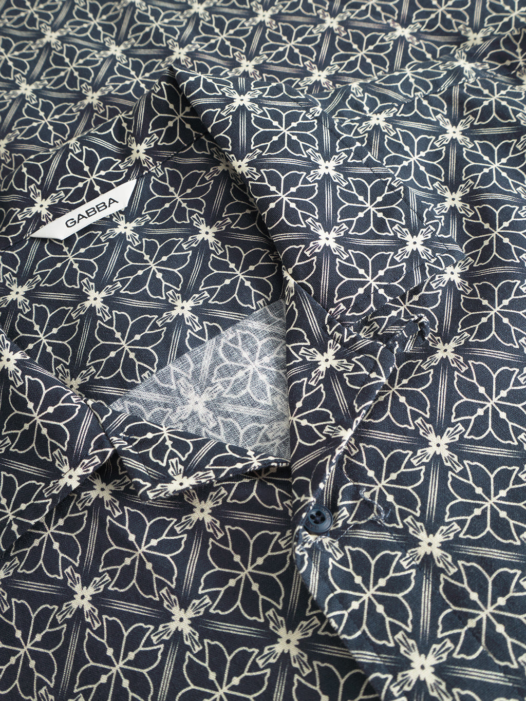 Close-up of the Gabba Timo Resort AOP SS - Navy shirt, featuring a dark blue pattern with white floral designs, crafted from a premium linen-cotton blend. The collar and button details accentuate the intricate fabric pattern and seasonal print.