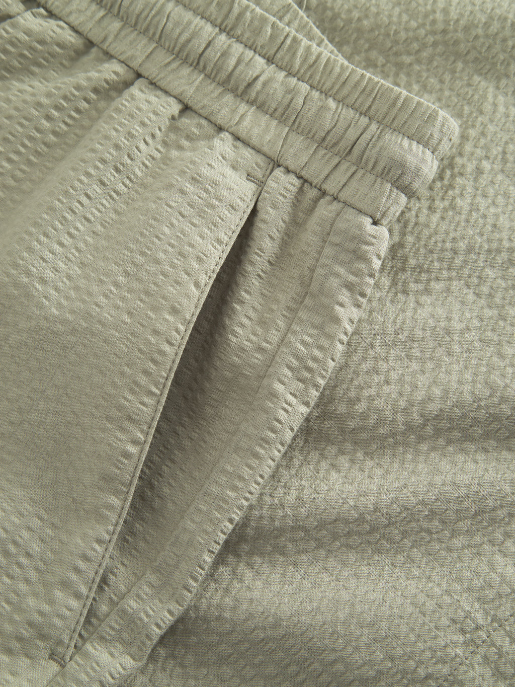 Close-up of Gabbas Tommi Seer - Green Sea pants in light green seersucker with an elastic waistband, side pocket, and 100% cotton dimpled fabric.