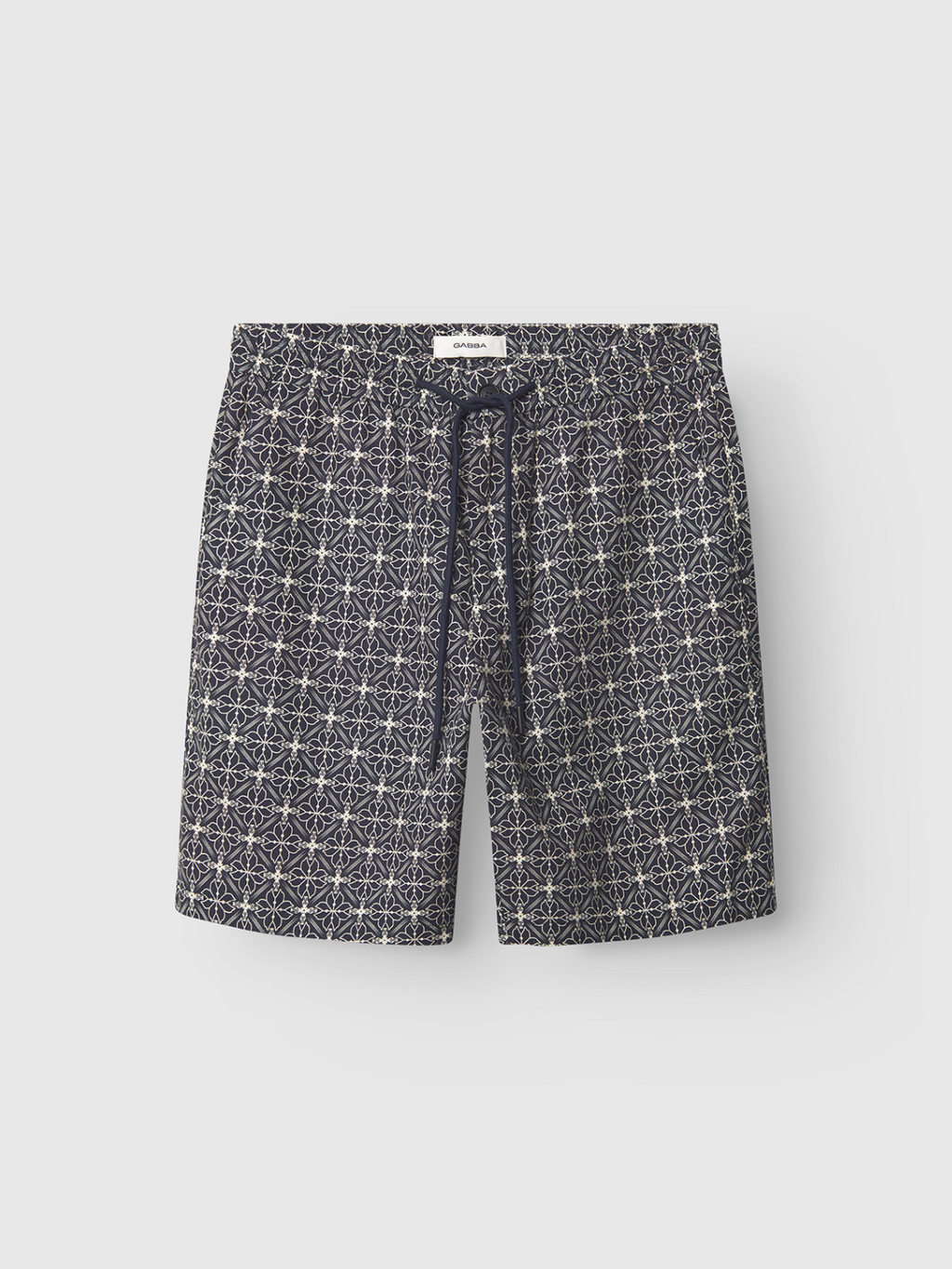 Gabba’s Tommi AOP - Navy swim shorts in 100% cotton feature a white geometric star pattern, elastic waistband, and black drawstring, shown against a plain white background.