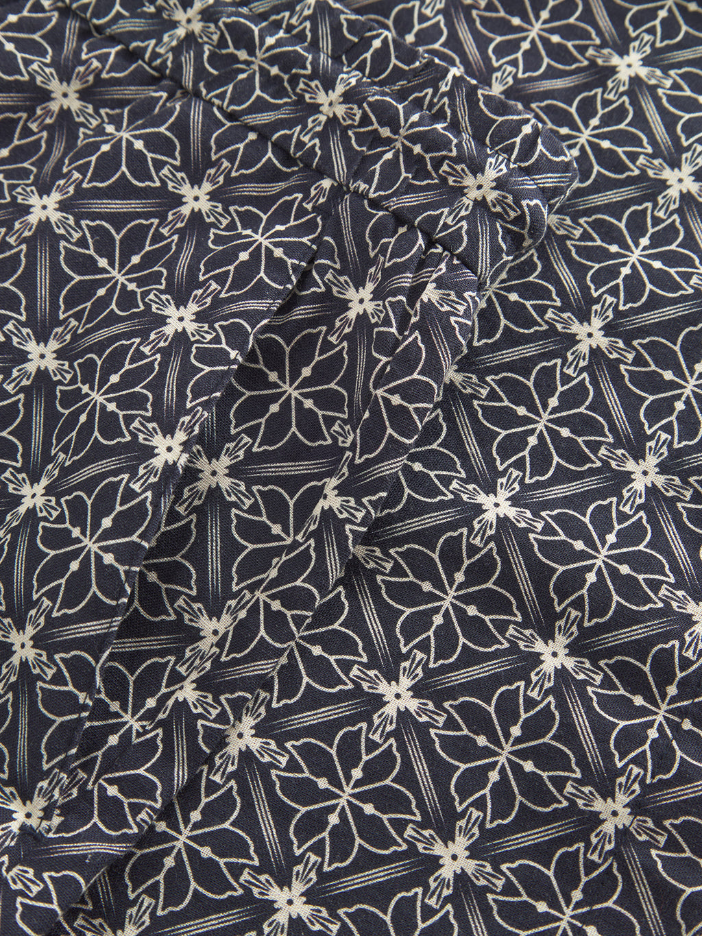 Close-up of Tommi AOP - Navy by Gabba, a dark blue cotton fabric with a white floral pattern featuring stylized flowers in squares, creating a geometric motif that suggests seersucker textures. Ideal for crafting chic shorts, the fabric has a slightly wrinkled appearance.