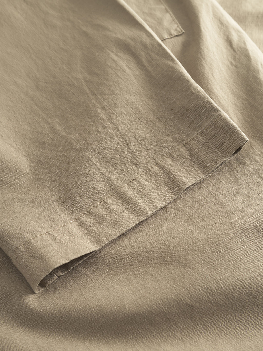 Close-up of Gabbas Topgun Jash - Sand, featuring beige fabric with subtle stitched seams reminiscent of technical pants. The lightweight texture mirrors the smooth surface of ripstop fabric, showcasing an intricate pattern.