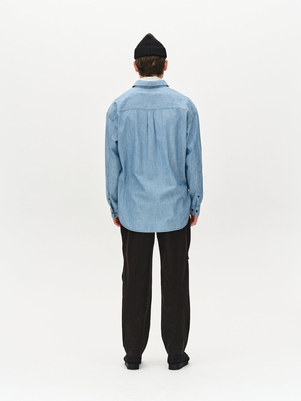 A person facing away wears a black Gabba Topgun Jash beanie, a light blue denim shirt, and black technical pants with an elastic waistband against a plain white background.