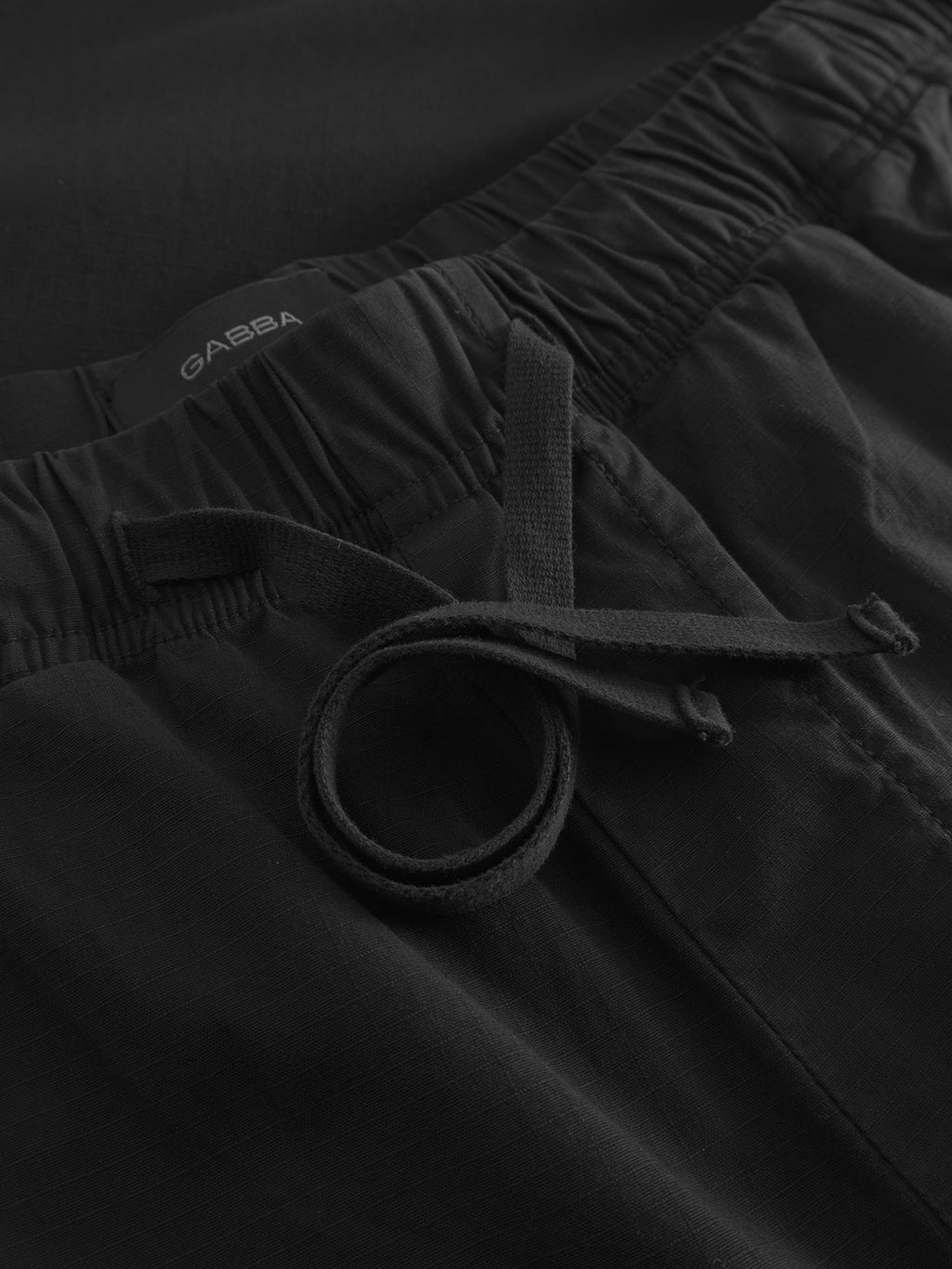 Close-up of Gabbas Topgun Jash - Black pants showcasing an elastic waistband with a tied drawstring. The smooth ripstop fabric is slightly textured for durability, and the brand tag is partially visible at the top.