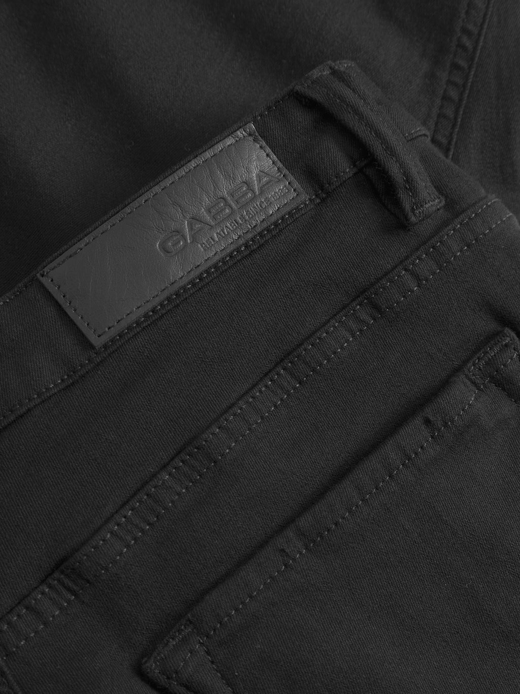 Close-up of Gabbas Jones Hold Black denim jeans showcasing a leather patch with embossed branding on the waistband. The super-stretch fabric ensures comfort, and visible stitching highlights craftsmanship. Reinforced pockets offer durability to their sleek design, and the jeans are neatly folded.