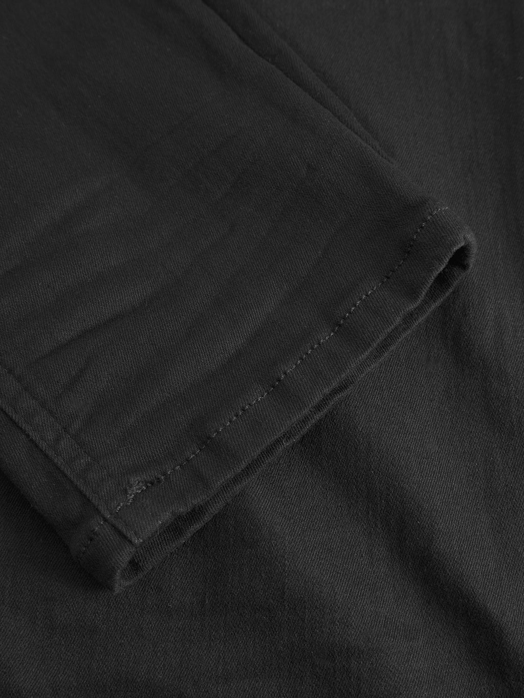 Close-up of the hem of a Gabba Jones Hold Black denim garment, highlighting visible stitching details. The smooth texture of the super-stretch fabric appears slightly folded, ensuring comfort and durability.