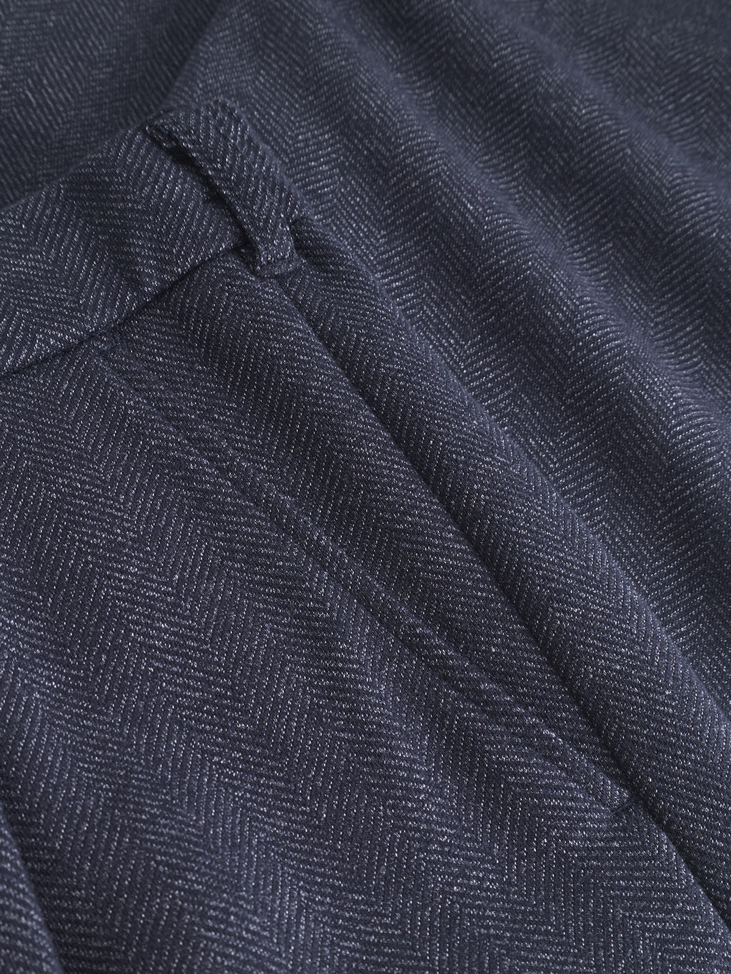 Close-up of Gabbas Napoli 19 Tweed - Navy, showcasing its classic dark gray herringbone pattern. The detailed texture and subtle sheen enhance its elegance. The folded fabric resembles tweed pants, creating shadows that highlight the intricate design.