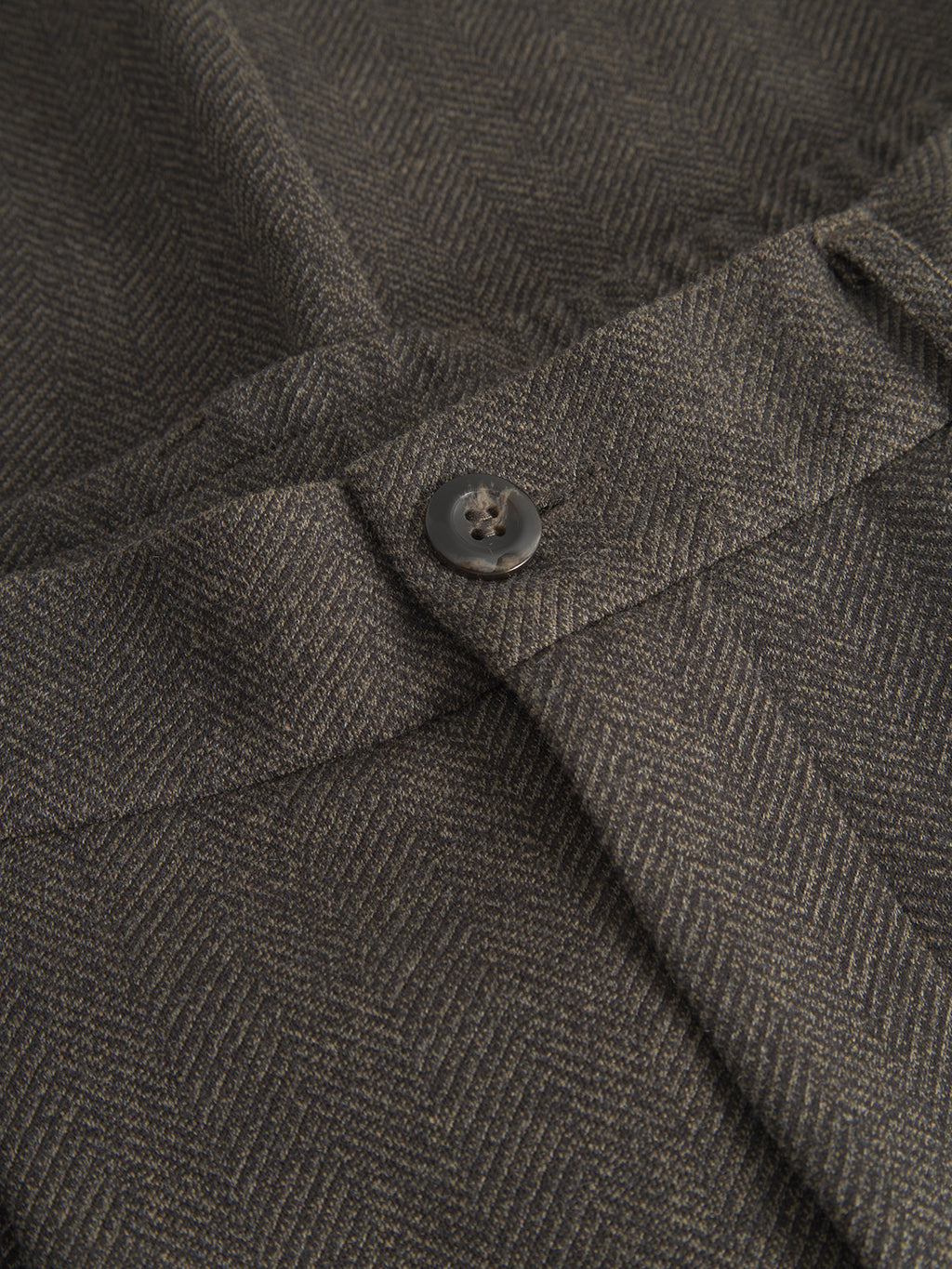 Close-up of the Napoli 19 Tweed by Gabba, featuring a textured fabric waistband with a glossy, dark button fastening. The pants showcase a herringbone pattern in gray and black for a classic, sophisticated look and perfect fit.