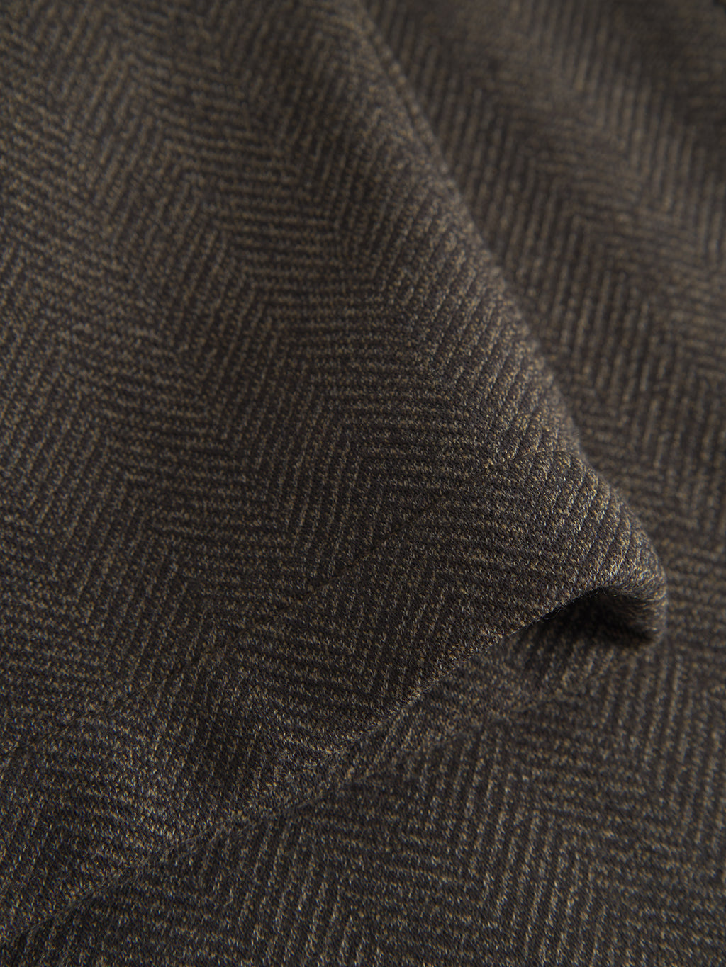 Close-up of Gabbas Napoli 19 Tweed - Brown fabric, showcasing a dark brown herringbone reminiscent of tweed pants. Fine diagonal zigzag patterns and soft texture create gentle folds, shadows, and highlights for a classic style.