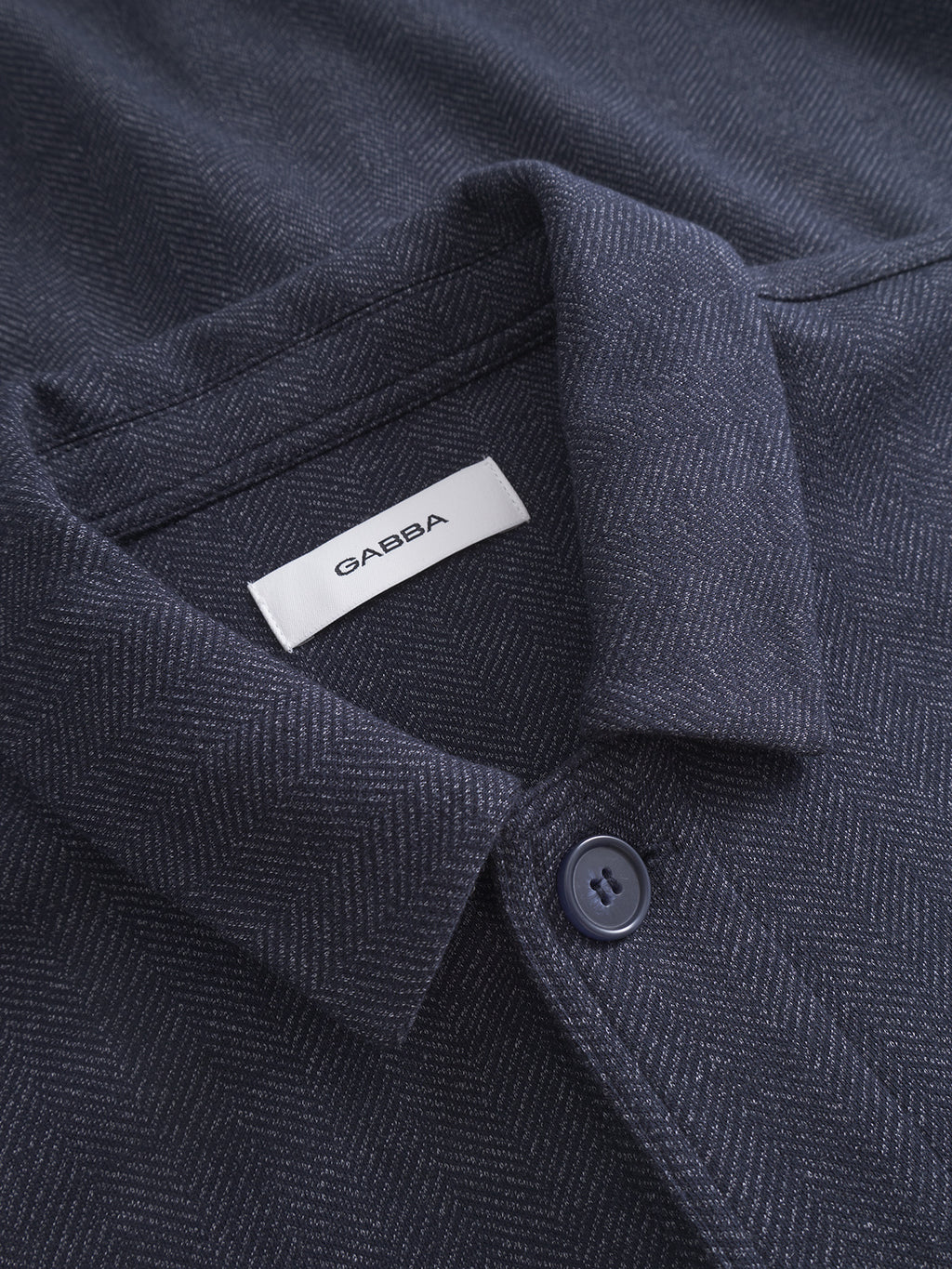 Close-up of the Peter Tweed - Navy shirt by Gabba, showcasing a dark blue button-down with a subtle herringbone pattern. The tailored fit highlights a single button near the collar and a small label reading GABBA for timeless style.
