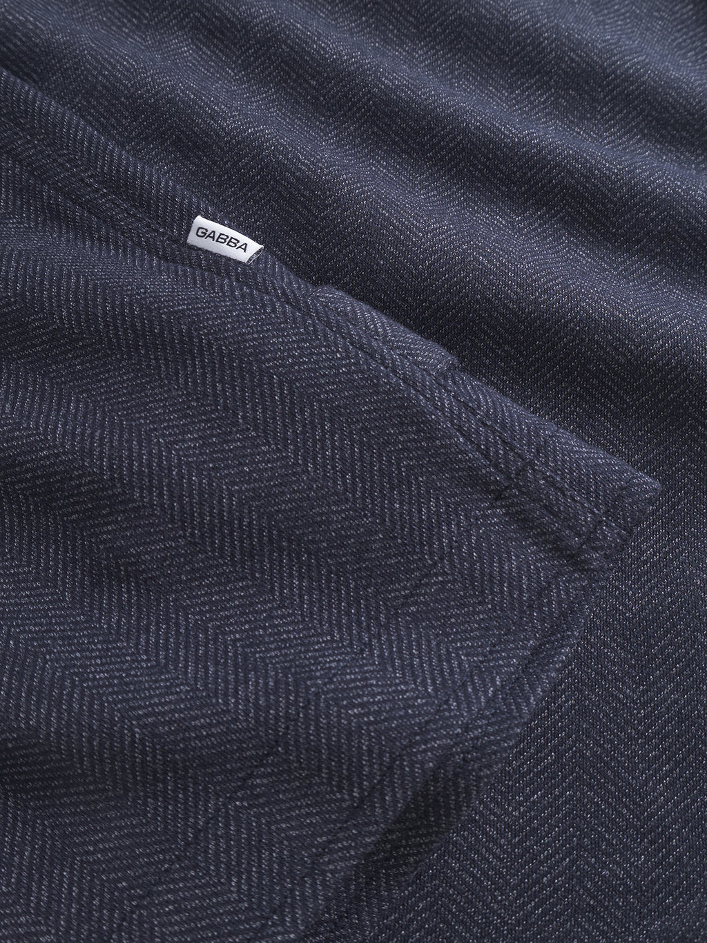 A close-up of dark blue fabric with a subtle herringbone pattern evokes timeless style akin to a classic tweed jacket. The fabric bears a small white label reading Gabba, showcasing the Peter Tweed - Navy product.