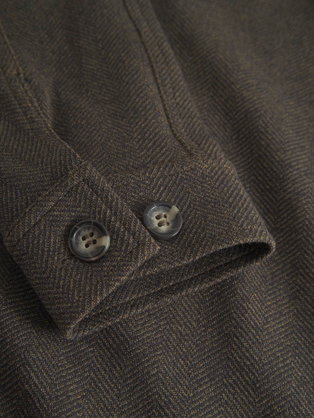 A close-up of the Peter Tweed - Brown sleeve by Gabba shows a herringbone pattern with two buttons. The detailed texture reflects a sophisticated design similar to a classic tweed jacket, exuding elegance and timeless style.