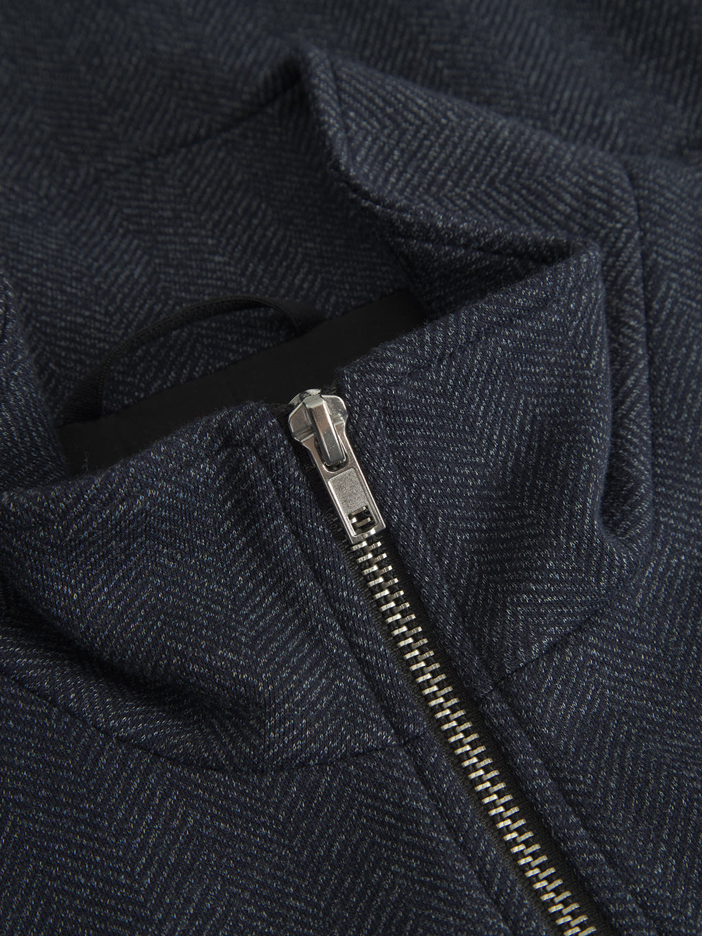 Close-up of Gabbas Nik Tweed - Navy jacket, featuring rich tweed fabric with a dark, textured herringbone design and silver zipper. A partially open zipper reveals a small black fabric loop beneath the collar for sophistication.