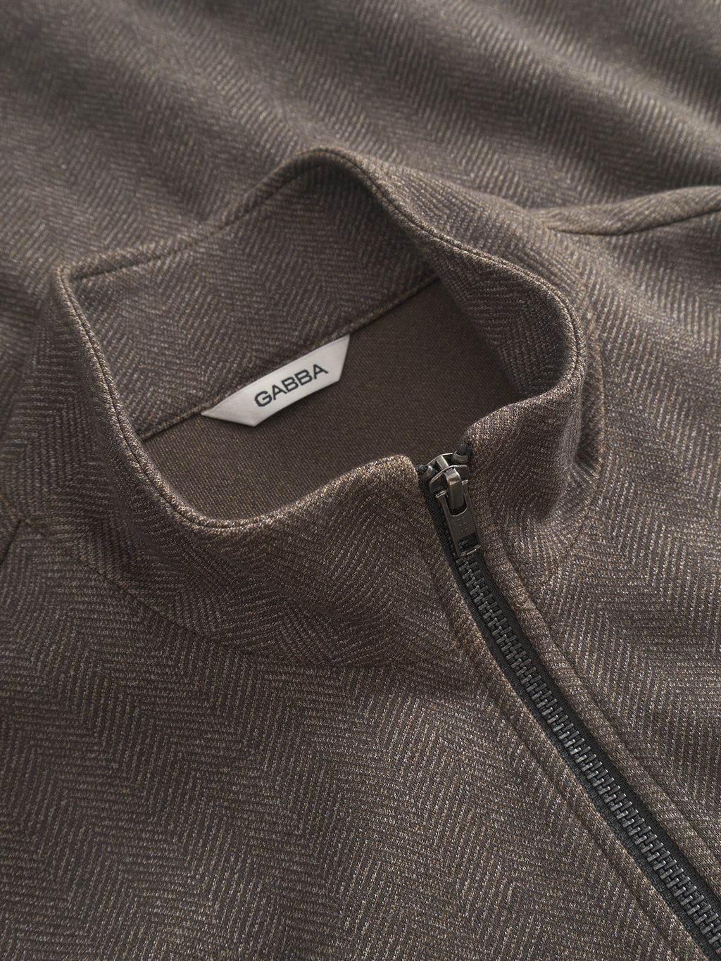 The Nik Tweed - Brown by Gabba features a detailed brown herringbone-patterned jacket with a high collar, black zipper, and visible tweed texture. Inside the collar, a white label displays Gabba, making it perfect for an everyday look.