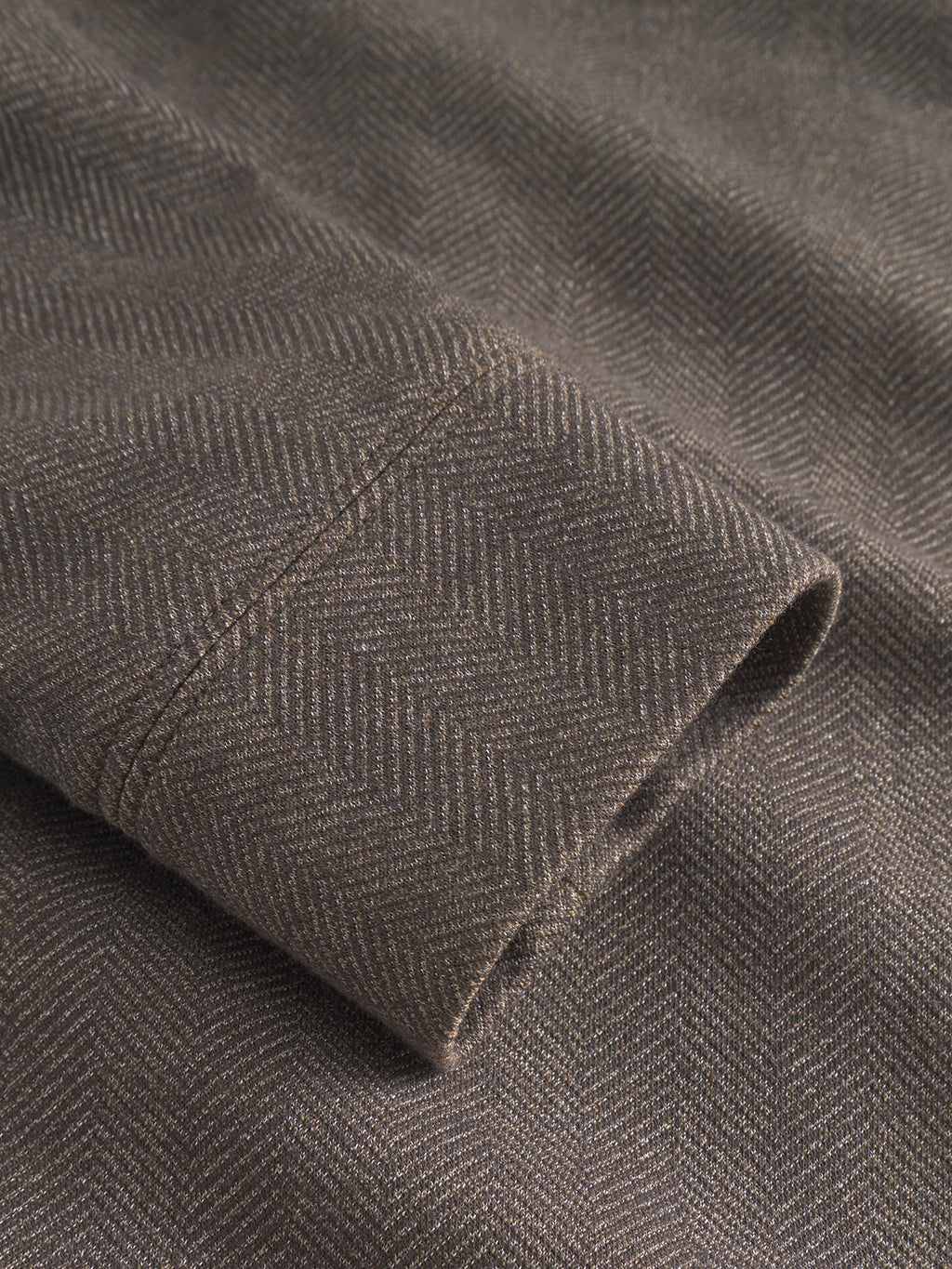 Close-up of Gabbas Nik Tweed - Brown fabric, showcasing its herringbone pattern. The material features a folded cuff with visible seam stitching, emphasizing its texture and detail, ideal for an everyday jacket layer.