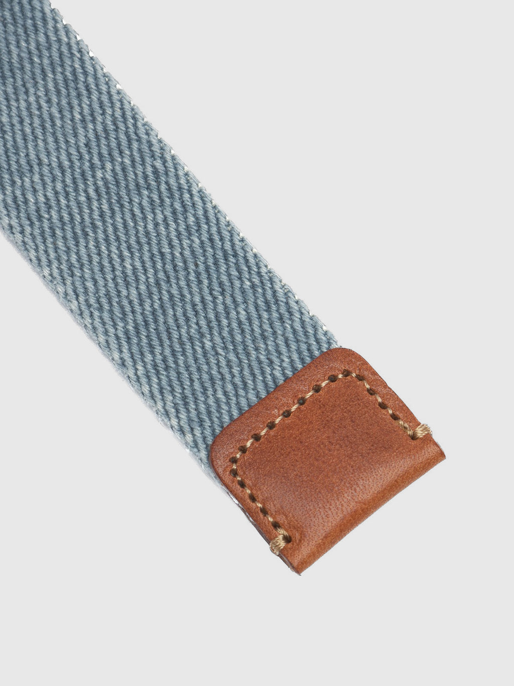 The Manica Denim Belt by Gabba features a high-quality light blue denim strap with a diagonal weave. It ends in a rectangular brown leather section, complete with visible stitching and rounded corners, beautifully contrasting the textured cotton and gleaming against the metal buckle.
