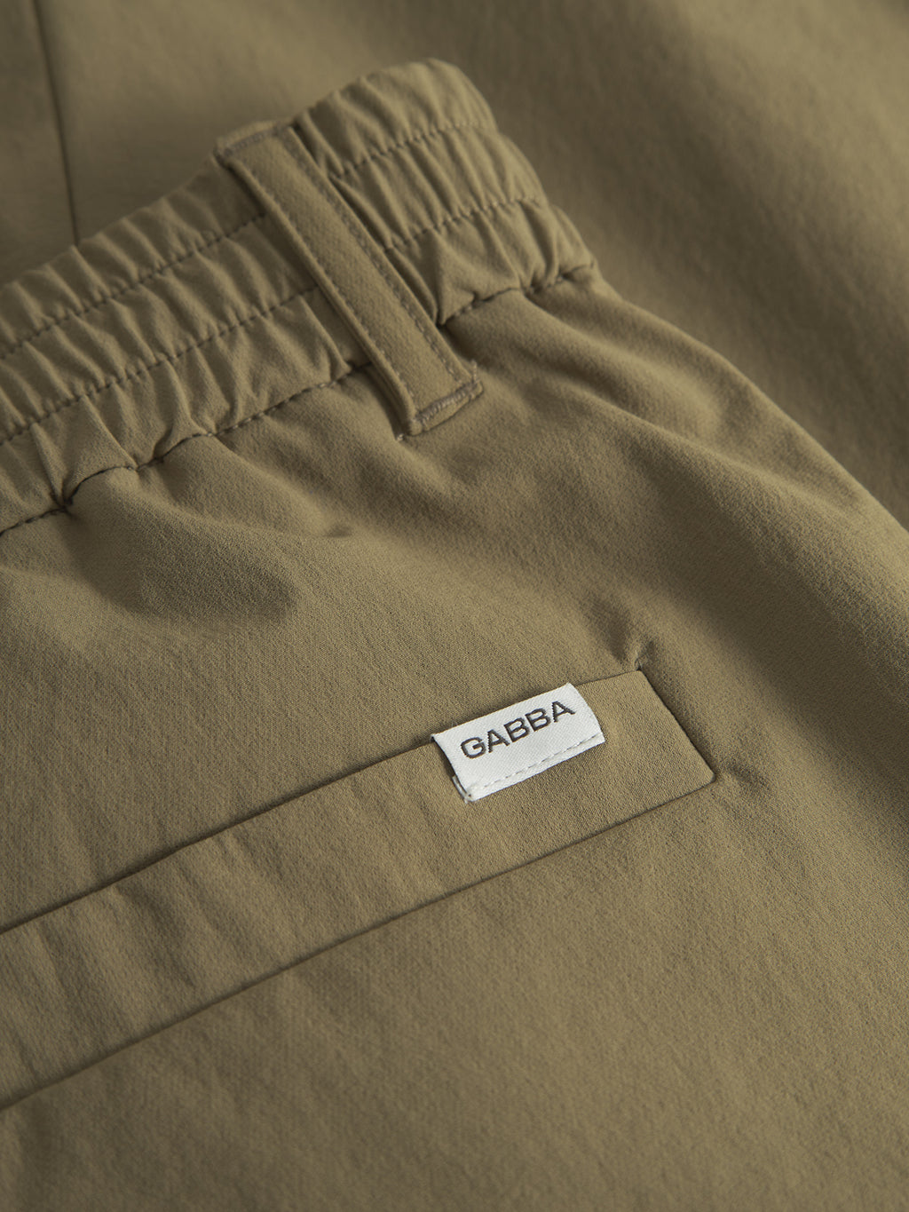 Close-up of Napoli 19 Tech - Army pants by Gabba, in olive green, featuring a versatile design with an elastic waistband and back pocket. A white label with GABBA in black lettering is above the pocket. The smooth, neatly stitched fabric ensures ultimate comfort.