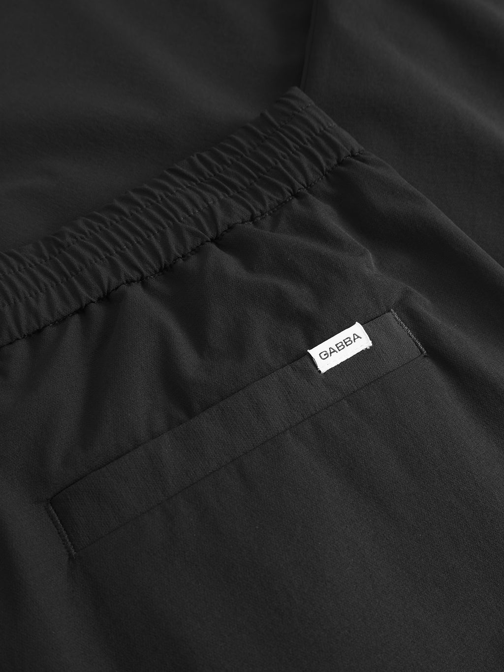 A close-up of Napoli 19 Tech - Black pants by Gabba highlights their versatile design featuring an elastic waistband and a back pocket with a small white tag. The smooth, slightly shiny fabric ensures effortless comfort.