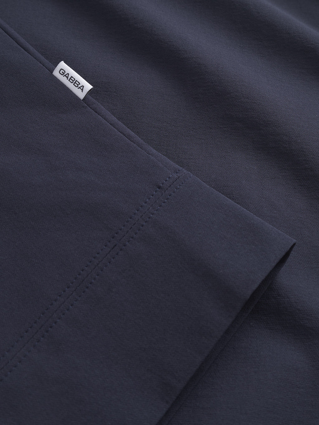 Close-up of Nik Tech - Navy fabric by Gabba, featuring dark navy tech material with visible stitching and a small white Gabba tag. The smooth, neatly folded fabric suits an on-the-go lifestyle.