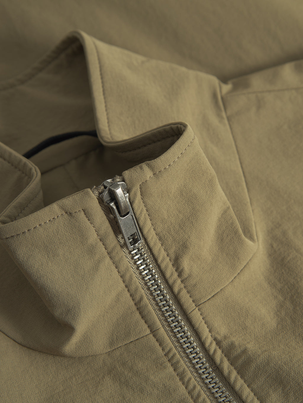 Close-up of the Gabba Nik Tech - Army jacket: a khaki-colored, zip-front design with advanced tech material. It has an open stand-up collar, smooth matte finish, and reveals the interior fabric—ideal for an active lifestyle.