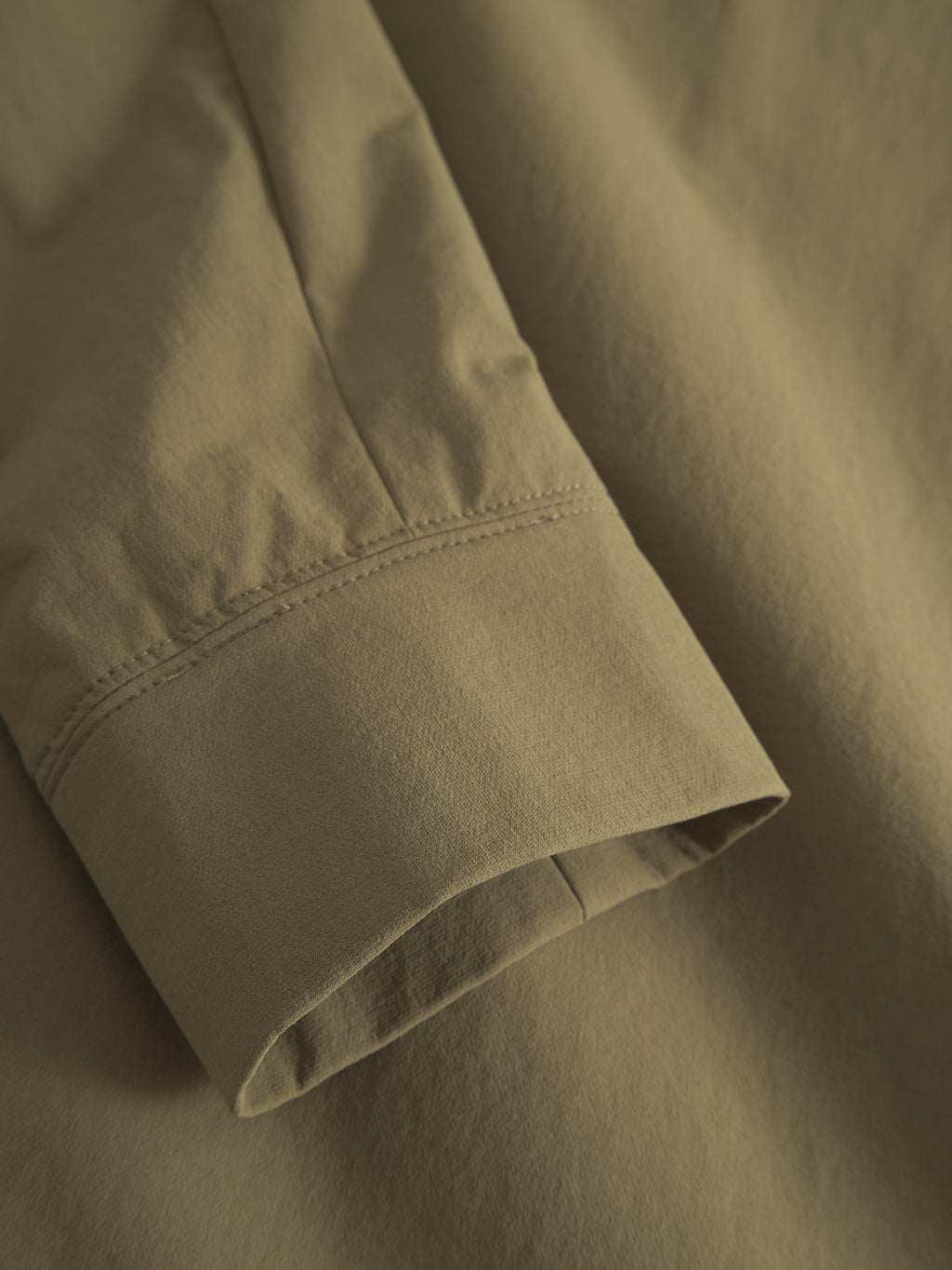 The close-up of the Nik Tech - Army by Gabba showcases its olive green long sleeves and neatly hemmed cuffs, highlighting the tech materials smooth texture. Designed for an on-the-go lifestyle, the fabric is slightly gathered at the seam.