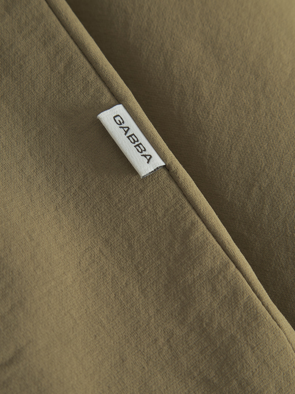A close-up of the Nik Tech - Army fabric features a visible seam with tech material, adorned with a small white tag reading Gabba, epitomizing an on-the-go lifestyle.