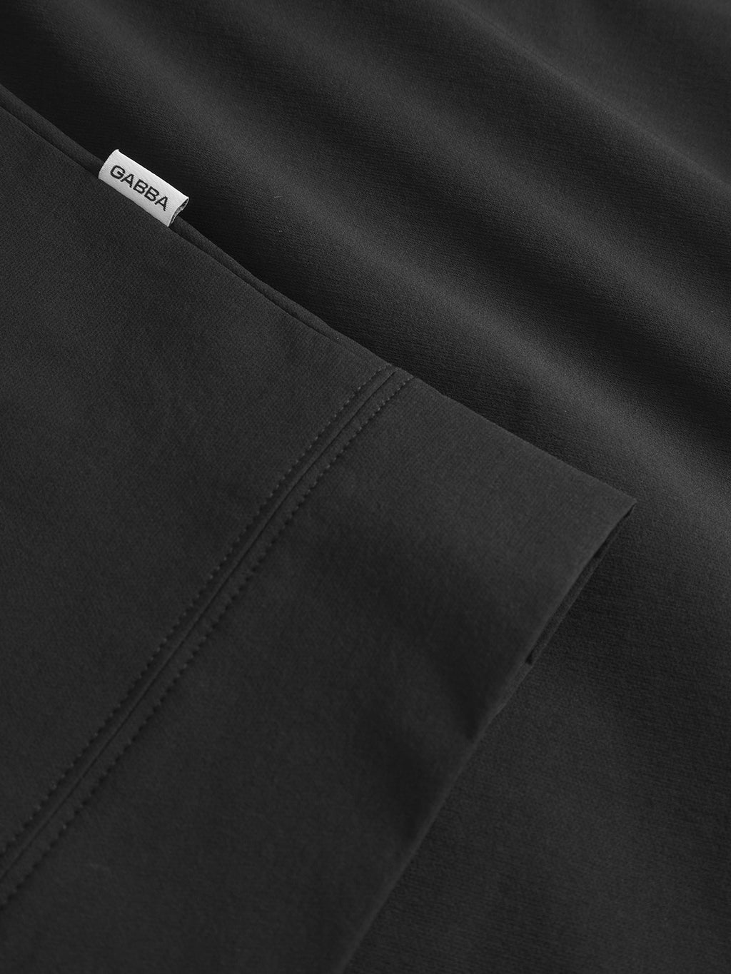 Close-up of Gabbas Nik Tech - Black fabric shows neat stitching and a white GABBA tag at the seam. The smooth, finely crafted material suggests a practical design ideal for an on-the-go lifestyle.