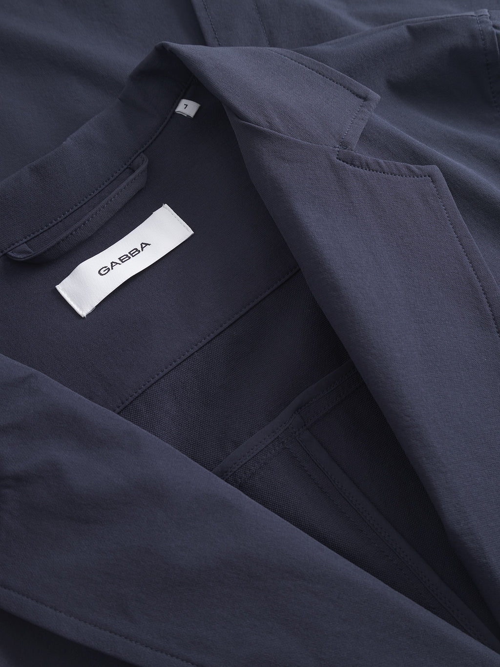 Close-up of the Plaza Tech - Navy jacket by Gabba, showcasing its fabric texture and stitching. The image features the collar, a spacious inside pocket, and a visible white label with Gabba in black text.