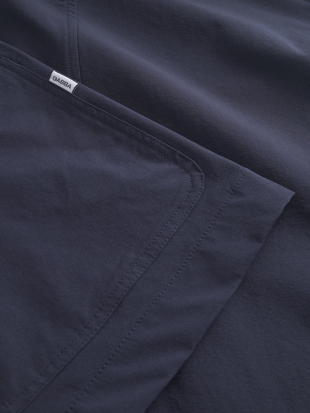 Close-up of a Plaza Tech - Navy jacket by Gabba, showcasing its smooth fabric and neatly stitched edges. The tailored fit and spacious pockets provide style and practicality. A small white label with text is sewn near a seam.
