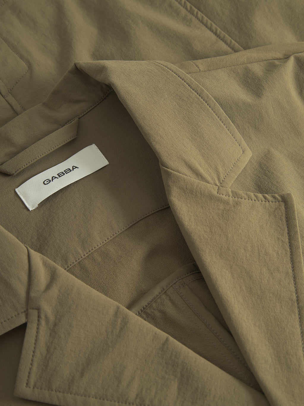 Close-up of the Plaza Tech - Army jacket by Gabba with a notched lapel, visible white inside label with Gabba, smooth texture, tailored fit, and spacious pockets for style and functionality.