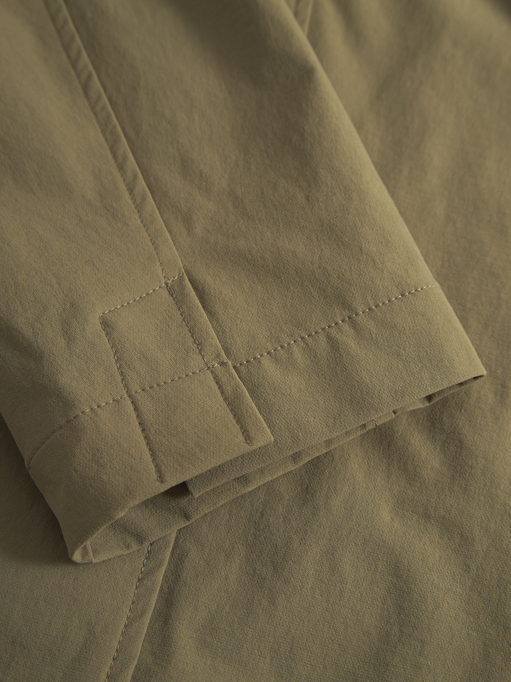 Close-up of army green fabric on a Gabba Plaza Tech jacket, showing two layers with visible stitching. The texture looks smooth and slightly matte, emphasizing the jackets tailored fit.